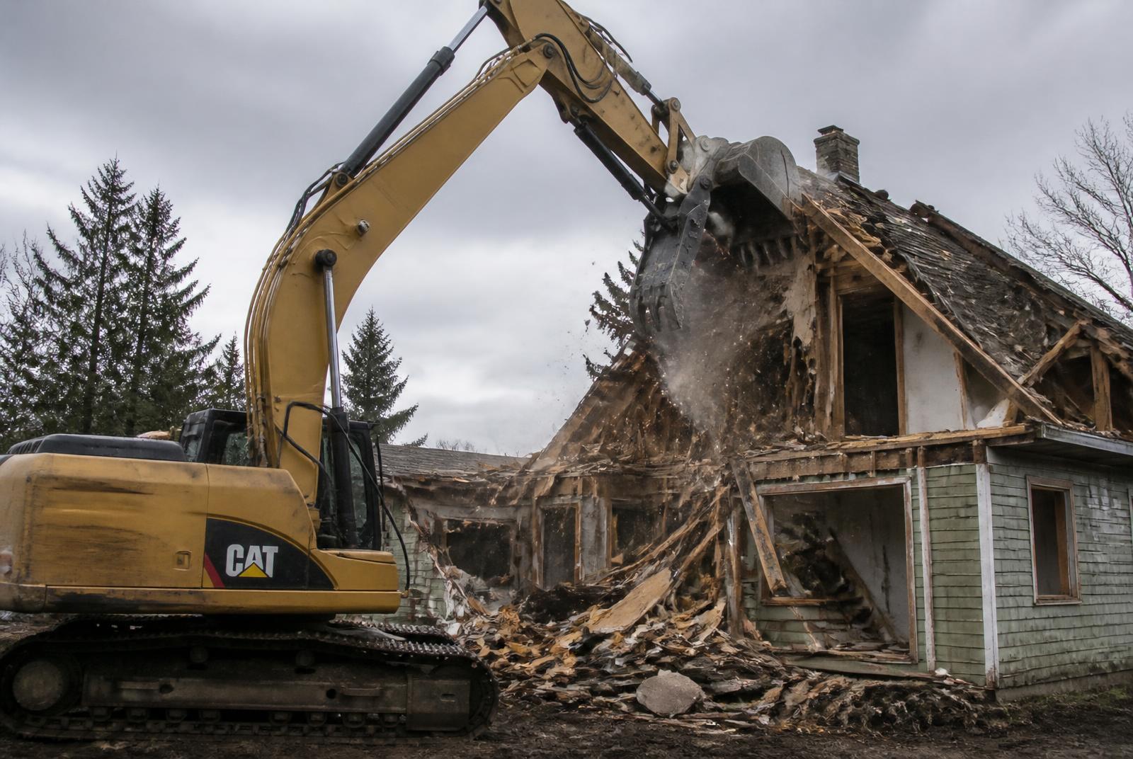 Excavator tearing down a house on a cleared lot